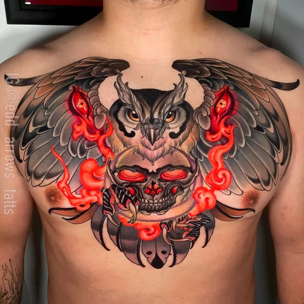Tatuaje de pecho: búho con alas abiertas sobre un cráneo, con llamas rojas, en neotradicional a color